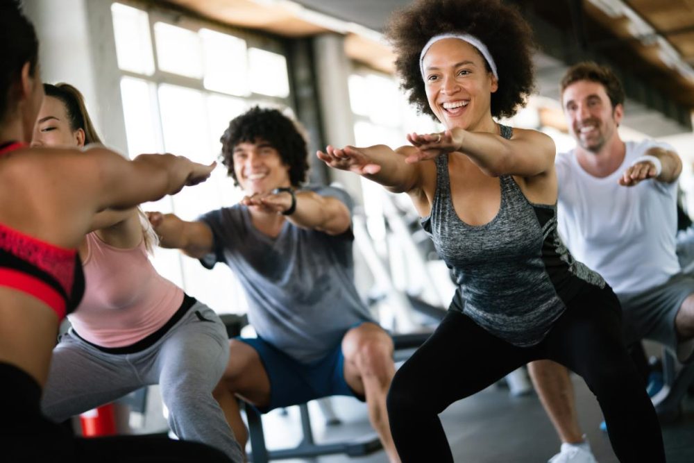 Cours collectif d’aérobie en train de faire des squats à l’intérieur d’une salle de sport.